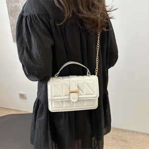 White quilted crossbody bag with gold chain strap shown on a model in a minimalist setting