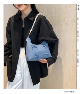 Blue denim underarm bag featuring delicate bows and a large pearl beaded strap detail