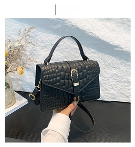 Detail of black crocodile texture handbag with gold metal clasp and V-shaped flap