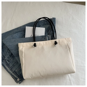 Close-up of cream puffer tote bag with black rope handles and adjustable drawstring detail