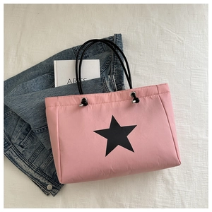 Pink nylon tote bag detail with black star print and metal eyelets on textured background