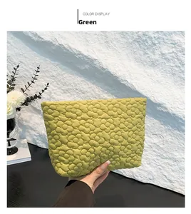 Detail shot of green quilted clutch bag with floral embroidery held against a textured wall