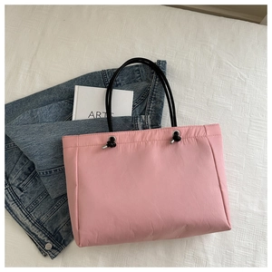 Detail of pink nylon tote bag featuring black rope handles and pleated texture surface