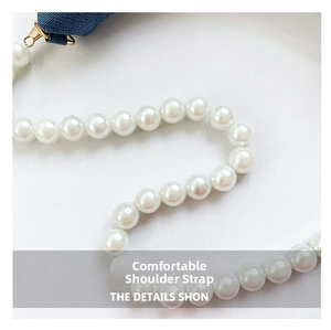 Detail of elegant faux pearl strap with golden metal rings and blue denim fabric texture