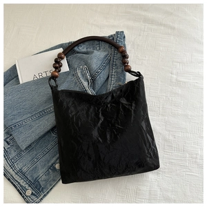 Detail of black pleated shoulder bag with dark brown wooden bead strap on white fabric