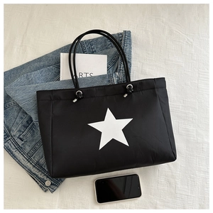 Detail of black tote bag featuring a white star pattern and silver metal eyelets