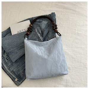 Detail of light blue pleated velvet bag featuring dark brown circular beaded handles and texture