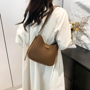 Minimalist brown matte leather bucket bag worn by model over a white coat outfit