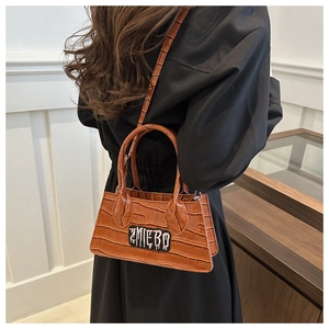 Brown crocodile pattern crossbody bag with letter patch shown on model's side