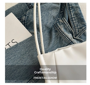 Dettaglio delle cuciture della borsa tote in pelle bianca su sfondo in denim blu
