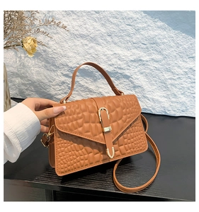 Detail of crocodile embossed leather texture on brown handbag with gold metal clasp