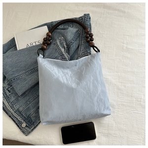 Detail of light blue wrinkled texture tote bag with dark wood bead handles on white background