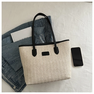 Detail of minimalist straw tote bag featuring black leather handles and trim accents