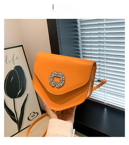 Détail d'un sac bandoulière orange avec boucle en strass tournesol et bandoulière cuir