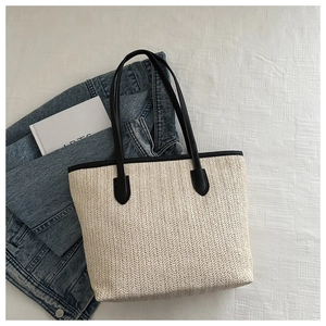Detail of cream straw tote bag with black faux leather straps styled on white fabric