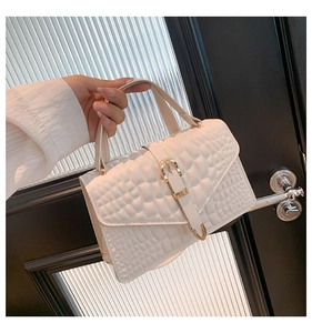 Close-up of white crocodile pattern handbag with gold metal clasp held by hand