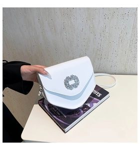 Détail du sac selle blanc avec boucle en strass étincelante et base incurvée chic