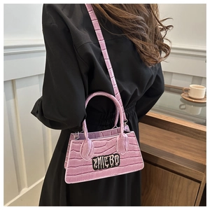 Side view of pink crocodile pattern crossbody bag with chain and brand lettering on model