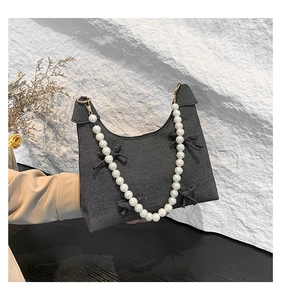 Detail of dark grey denim handbag with pearl chain handle and bow accents