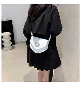 Détail d'un sac selle blanc avec boucle en strass sur un trench-coat noir chic