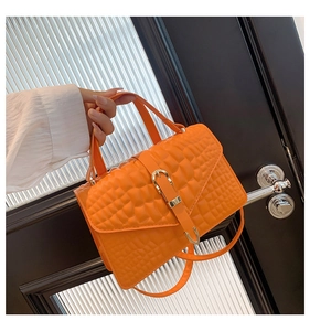 Detailed shot of orange textured leather crossbody bag with elegant gold clasp and handle
