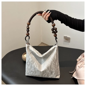 Detail of silver pleated fabric bag with dark brown wooden beaded handle on black surface