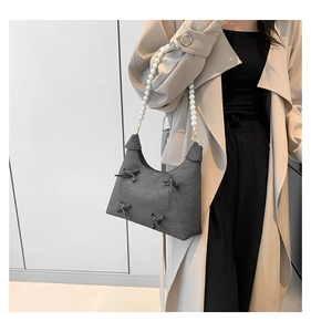 Detail of grey velvet shoulder bag featuring bow accents and elegant pearl strap