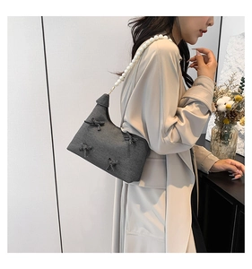 Detail of dark gray tote bag with elegant white pearl strap and decorative bows