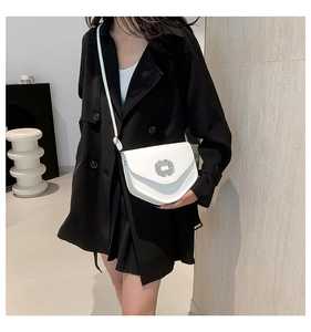 Gros plan d'un sac bandoulière blanc avec boucle à strass porté par un mannequin en noir