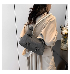 Close-up of gray denim tote with bow details and white pearl beaded shoulder strap