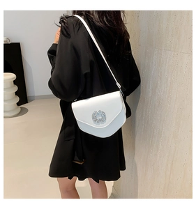 Détail d'un sac selle blanc avec boucle en strass sur fond de manteau noir élégant