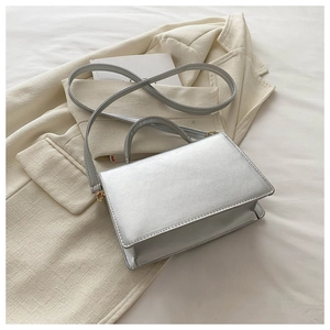 Detailed shot of silver metallic leather handbag with gold hardware on white blazer