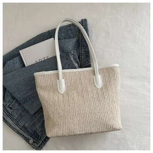 Close-up of beige woven tote bag with white leather straps and textured straw pattern