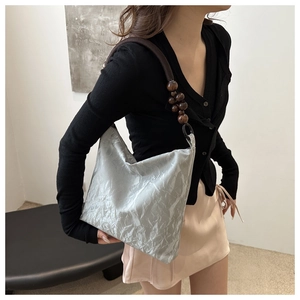 Close-up of silver pleated fabric shoulder bag with wooden bead strap detail