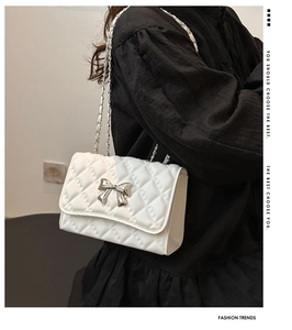 Close-up of white quilted bag with silver bow buckle and woven chain shoulder strap