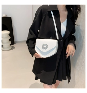 Gros plan d'un sac selle blanc avec une boucle en strass et une fine bandoulière élégante