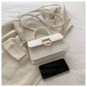 Dettaglio macro della mini borsa quadrata bianca con fibbia a D dorata su sfondo blazer