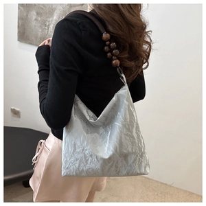 Close-up of silver-gray pleated velvet tote bag featuring decorative wooden beads on the strap