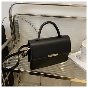 Detail of a black matte leather handbag with gold metal bar on a minimalist shelf