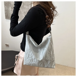 Detail of silver metallic hobo bag featuring dark brown wooden bead shoulder strap accent