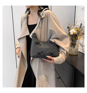 Detail of gray textured shoulder bag featuring chic bow accents and pearl bead strap
