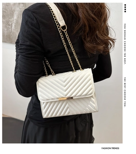 Rear view of a white V-quilted shoulder bag with gold chain strap on a black top