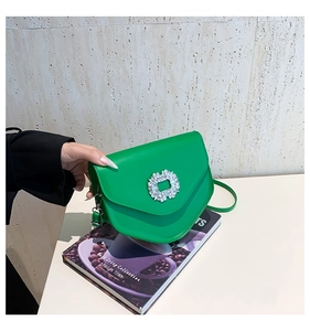 Détail du sac selle vert avec boucle en strass étincelante posé sur un magazine
