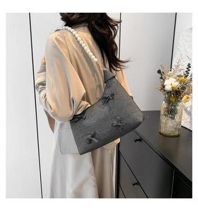 Detail of grey fabric shoulder bag with handmade bows and elegant pearl strap