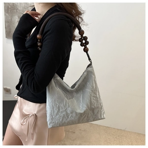 Detail view of silver pleated velvet shoulder bag with large brown wooden bead strap