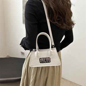 White crocodile pattern crossbody bag with letter patch shown in a modern lifestyle setting