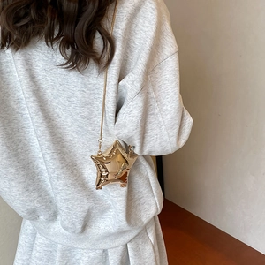Mini borsa a tracolla dorata a forma di stella con catena sottile su felpa grigia