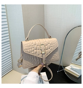 Detail of beige crocodile pattern handbag with gold hardware and removable strap