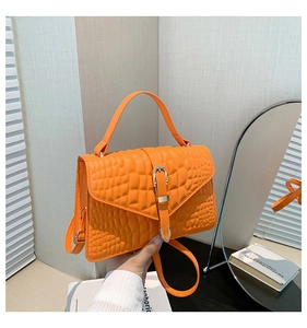 Detailed view of vibrant orange crocodile texture handbag with metallic buckle and shoulder strap