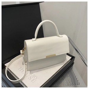 Close-up of white leather handbag with gold metal clasp on a luxury book display